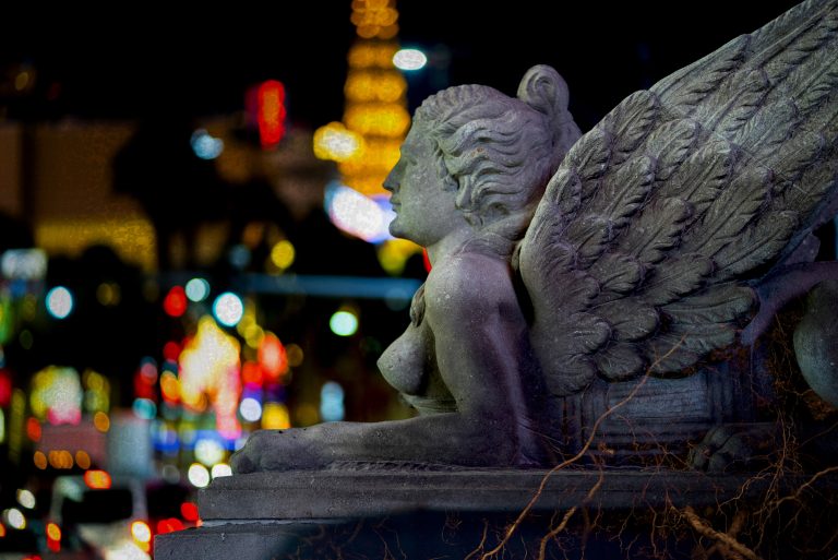 A reclining stone angel with paws... stands guard over a blurry background of the Las Vegas strip.